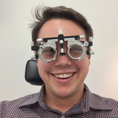 John Marc at the optometrist, wearing trial frames with a big smile